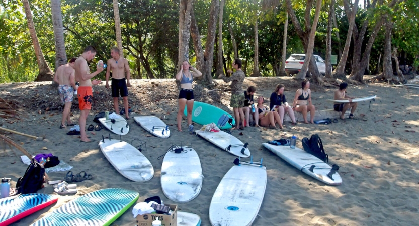 A group of students stand and sit near beached surfboards. 